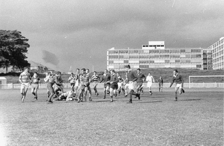 A game of rugby between Medicine II and Medicine III played on Randwick Oval with the Wallace Wurth School of Medicine and School of Biological Sciences Building in the background, 1963. (Photographer: D. Smith, UNSW Archives CN944/194)